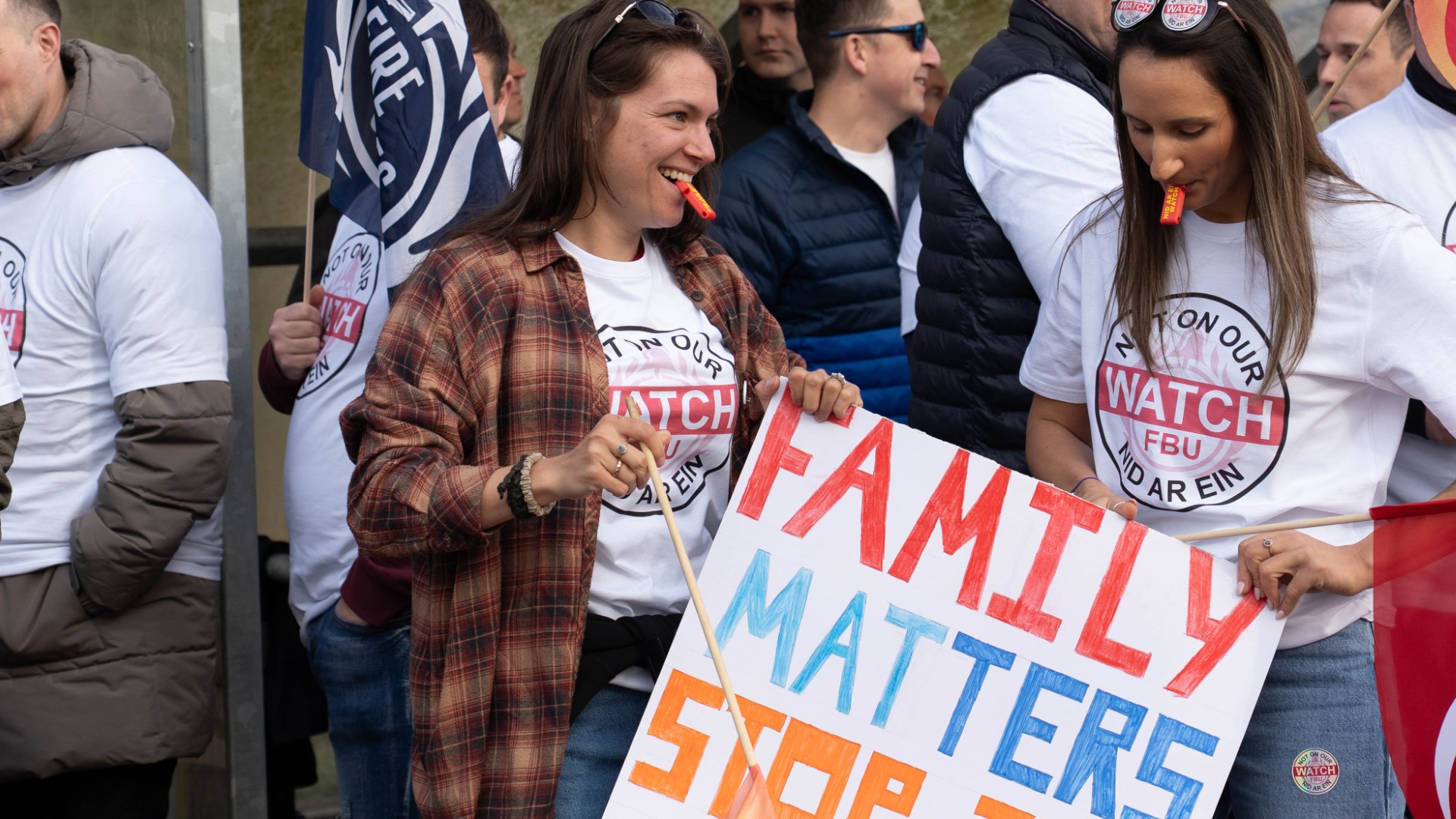 Two women wearing 'Not on our watch' t shirts with whistles and placards at a rally