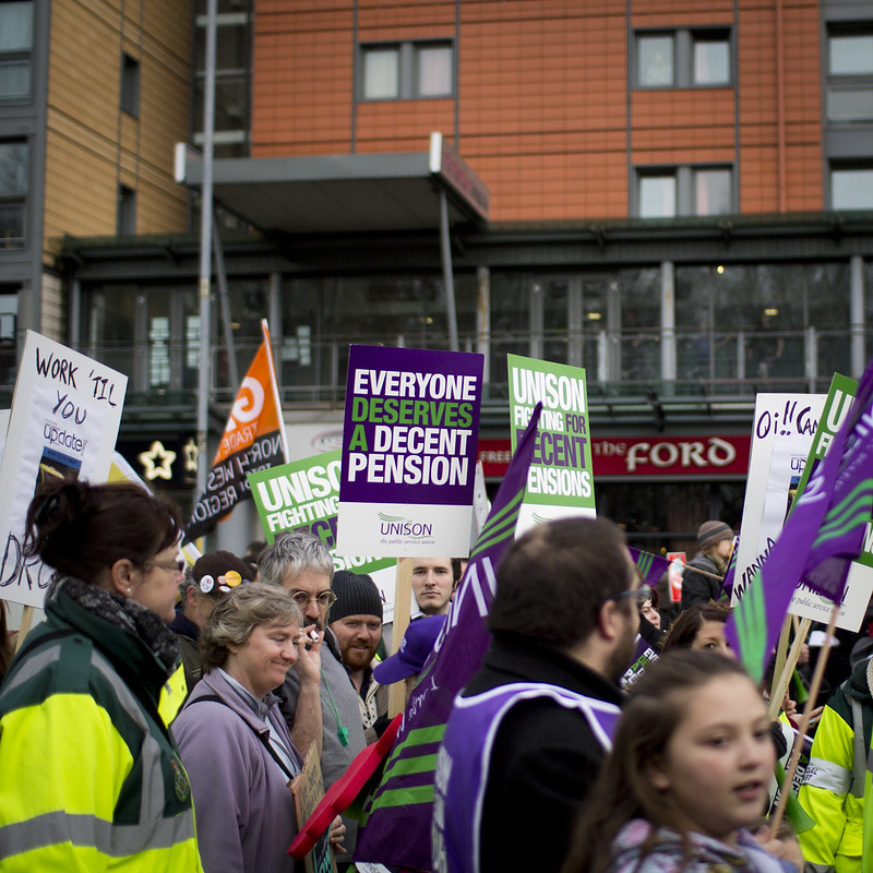 Crowd with people holding signs reading 'everyone deserves a decent pension'