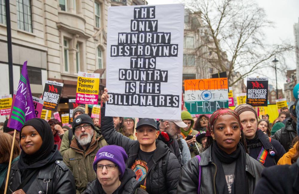 People at a protest against racism holding a placard reading 'the only minority destroying this country are the billionaires'