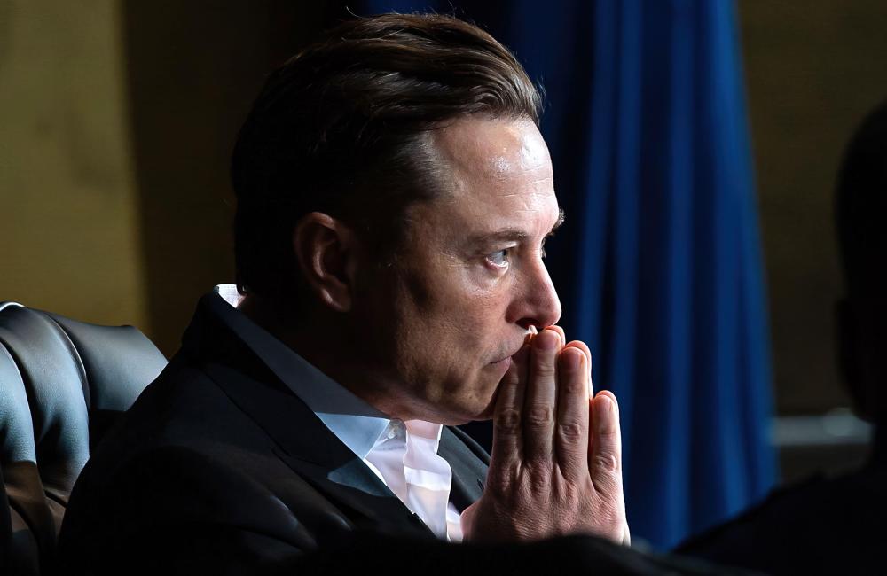 Elon Musk thinking and looking forwards with his hands up to his mouth