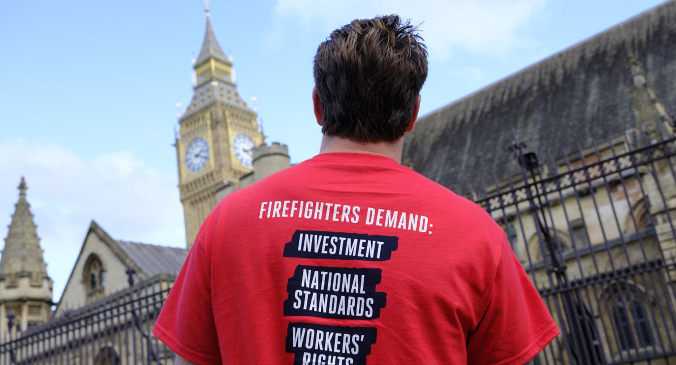 Firefighter outside parliament wearing t shirt reading 'Firefighters demand investment, national standards, workers rights'