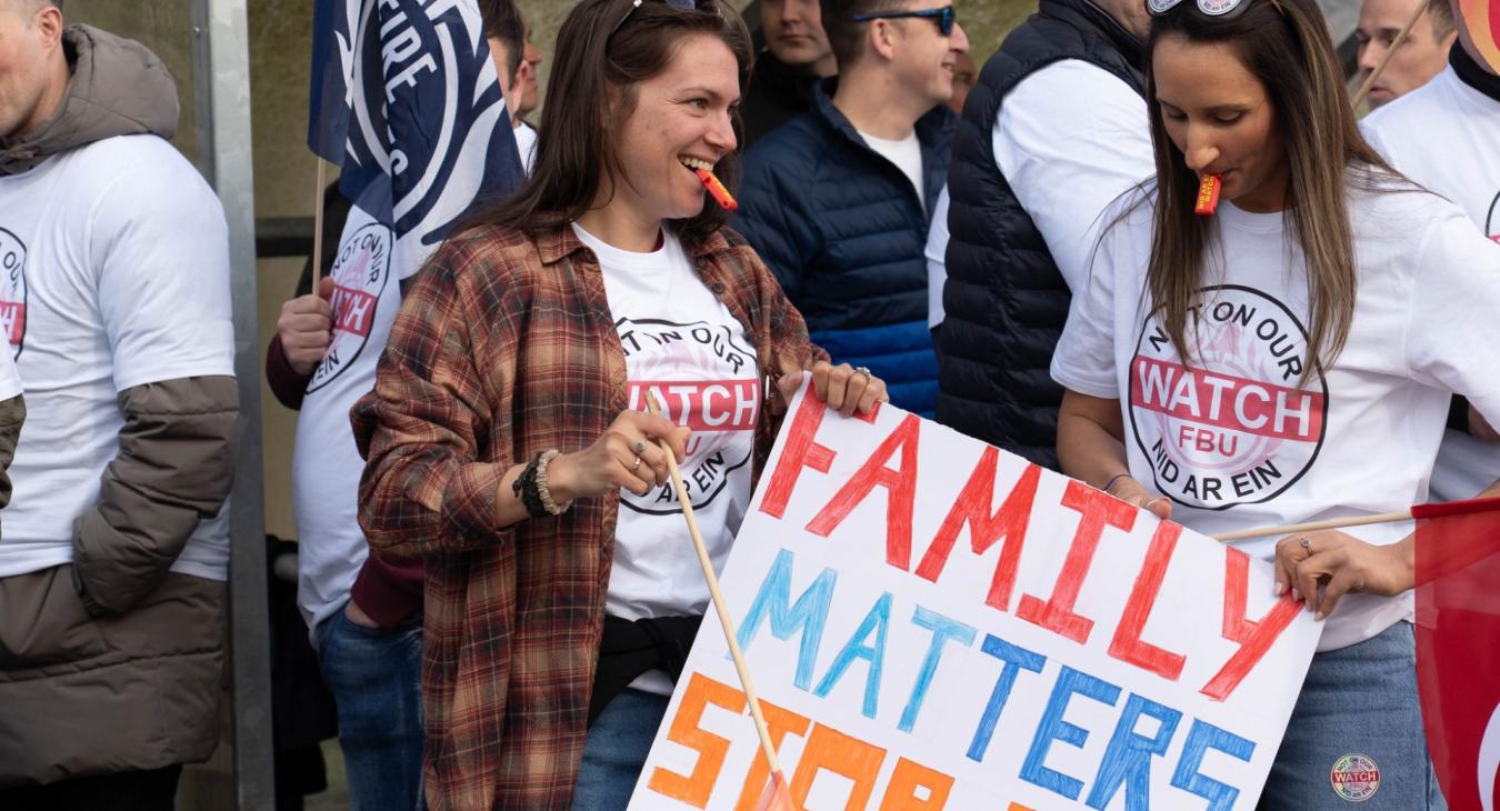 Two women wearing 'Not on our watch' t shirts with whistles and placards at a rally