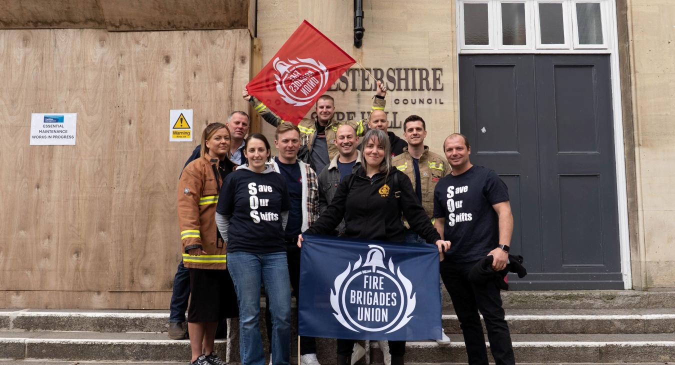 A group of FBU members hold flags outside Gloucestershire county council building